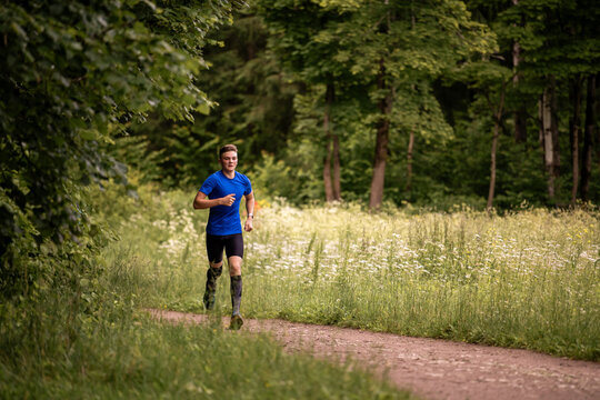 Young caucasian man running through green summer forest park.