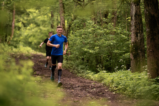 Young caucasian man running through green summer forest park.
