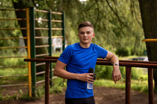 young caucasian man in a blue shirt holding a water bottle outdoors