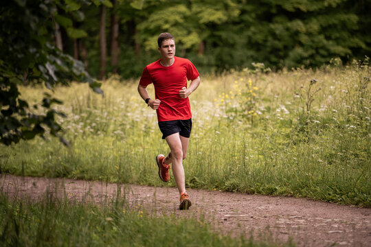 Young caucasian man running through green summer forest park.