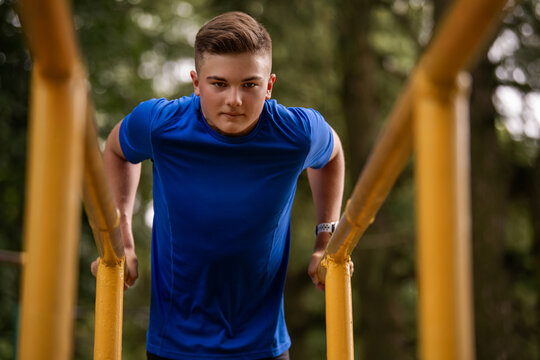 boy doing parallel bar dips outdoors. Summer sports activity.