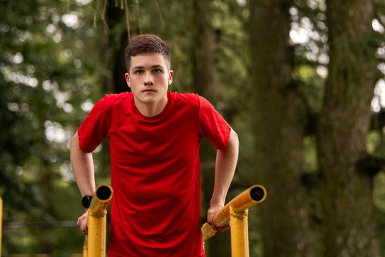 boy doing parallel bar dips outdoors. Summer sports activity.