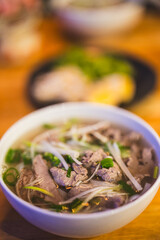 Close-up of a bowl of hot Vietnamese pho with beef, rice noodles, scallions and herbs. Traditional Asian cuisine – fresh, flavorful and comforting dish served warm.