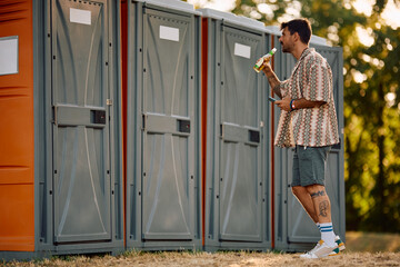 Young man waiting in front of portable toilet during summer music festival.