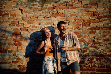 Happy couple of festival goers using cell phone against brick wall.