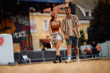 Happy couple of festival goers holding hands while walking by music stage.