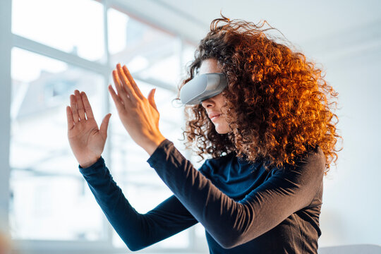 Young businesswoman with curly hair wearing virtual reality simulator gesturing in office