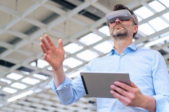 Businessman wearing virtual reality simulator gesturing and holding tablet PC at industry