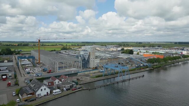 Aerial drone view of an industrial site in Alphen aan den Rijn next to a canal with cranes, factories and warehouses.