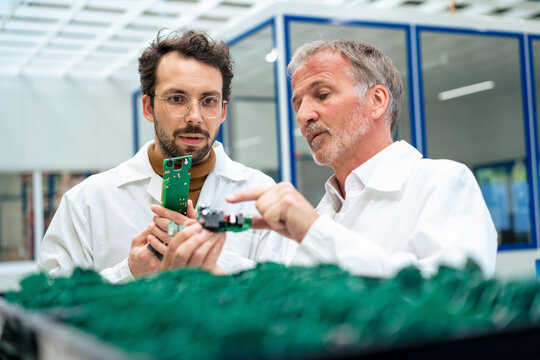 Senior engineer discussing over circuit board with colleague at industry