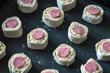 Sausages wrapped in raw puff pastry on a baking mat, ready to bake in the oven.