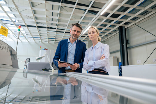 Confident mature businessman with colleague examining 3D printing machine at factory