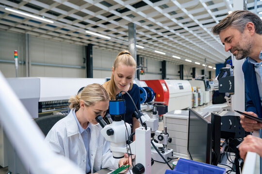Scientist looking through microscope with colleagues standing by in industry