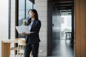Businesswoman holding laptop and looking out office window