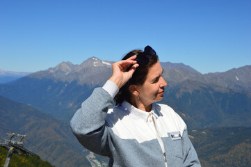 A Caucasian woman stands on a background of a beautiful mountain landscape. A brunette woman in sunglasses looks into the distance on vacation. Portrait of a female traveler.