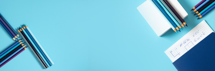 Top view of colored pencils, graph paper, and school notebooks on a blue desk. A vibrant and clean layout capturing the spirit of back-to-school and educational readiness.