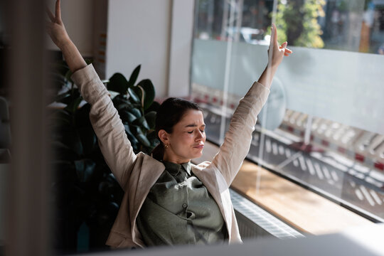 Businesswoman with arms raised gesturing in office seen though glass