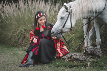 Young woman in traditional attire feeding a white horse outdoors