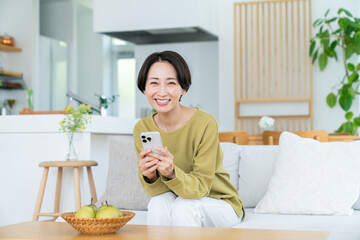 リビングでスマホを見るミドルの女性