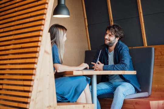 Smiling business people sitting with laptop and talking in office cubicle