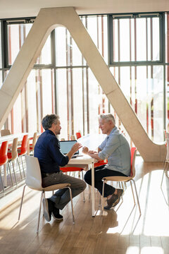 Senior businessmen discussing and sitting with laptop in office cafeteria