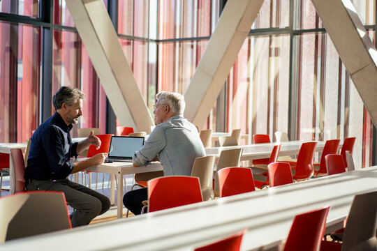 Senior businessman discussing and explaining colleague at table in office