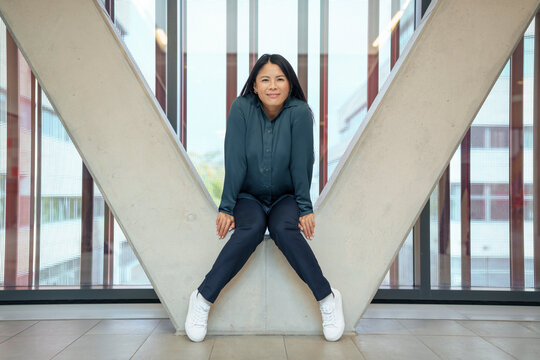 Smiling businesswoman sitting on architectural column in office