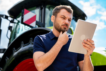 Focused man reading tablet with tractor in background at agricultural dealership