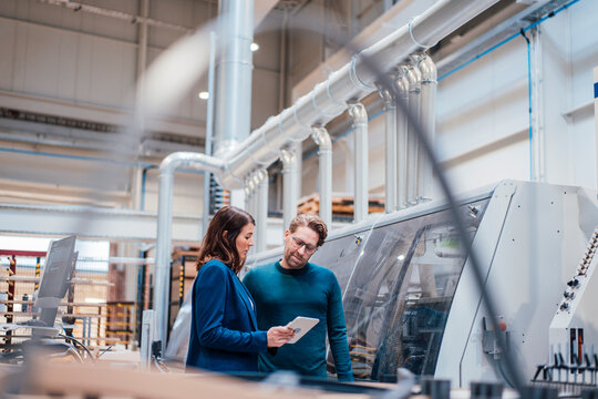 Engineer sharing tablet computer with colleague by machinery in industry