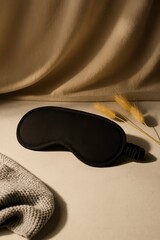 A close-up studio shot features a sleek black eye mask, lying serenely amidst a backdrop of neutral fabric. The setup conveys a sense of calm, relaxation, and tranquility.