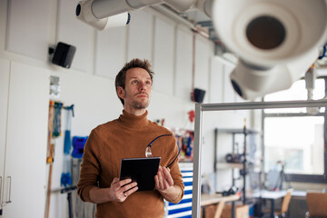Businessman holding tablet PC and looking at extraction arm in workshop