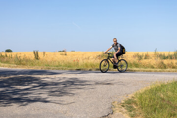 man cycling toward road junction with tree shadows in rural summer landscape