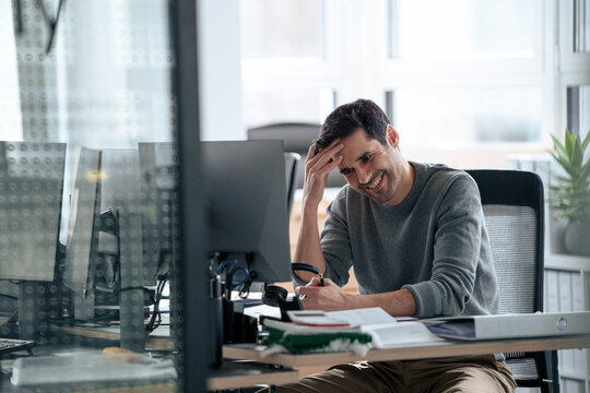 Happy mature businessman sitting near computer at desk in office