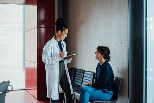 Happy doctor discussing with patient on chair in hospital
