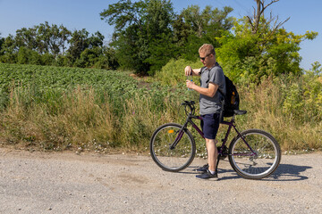 man standing with bicycle opening water bottle in green rural setting

