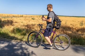 Obraz premium man holding water bottle cycling beside golden wheat field on summer day
