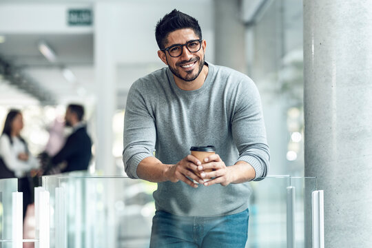 Happy businessman with coffee cup leaning on glass railing
