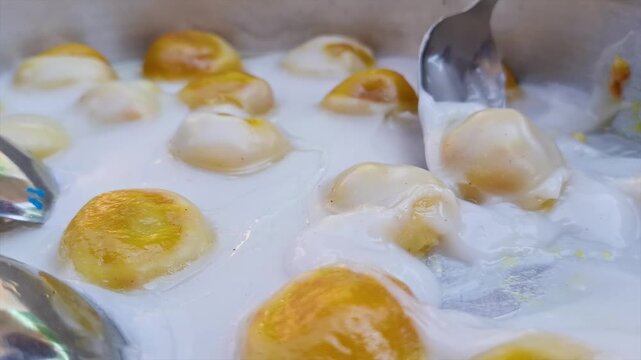 Close-up footage of Bugis Telanjang, a traditional Indonesian dessert made from glutinous rice flour dough filled with sweet coconut, served in rich coconut milk sauce
