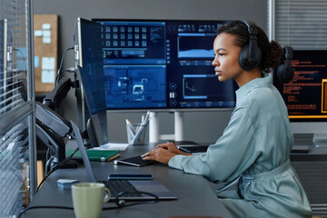 Young computer programmer wearing wireless headphones working on desktop PC