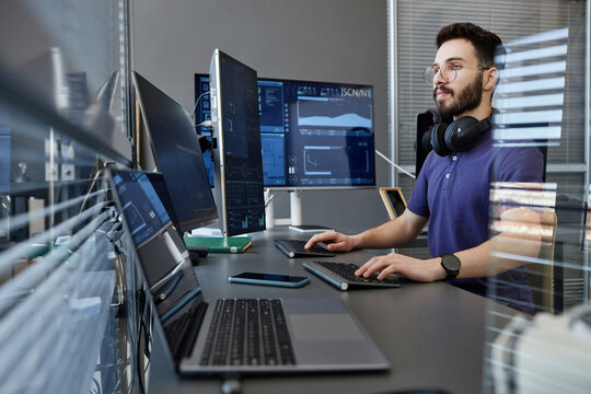 Young computer programmer with wireless headphones working on desktop PC