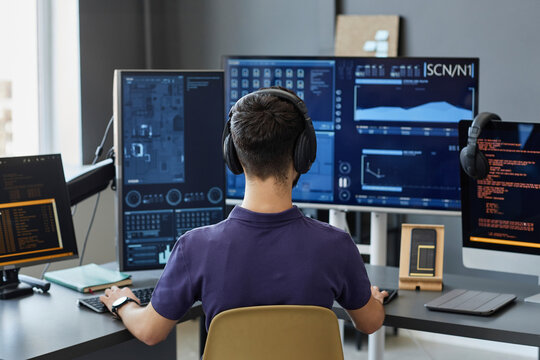 Young IT professional wearing wireless headphones working on computers
