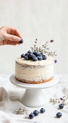 Close-up of interaction as fruit is arranged atop a buttercream cake. Natural light, ivory tones, and linen textures enhance the elegant presentation.