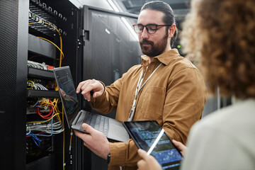 IT professionals discussing over data on laptop and tablet PC in server room