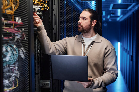 IT professional holding laptop and examining cables in server room