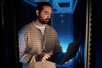 Young IT professional using laptop and working in data center