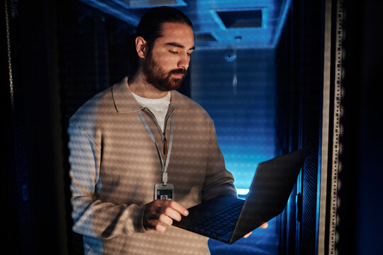 Young IT professional using laptop and working in data center