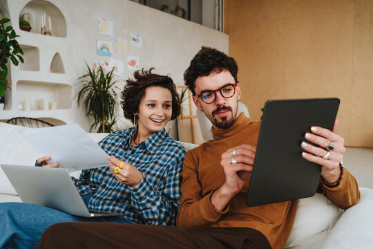 Illustrator explaining colleague over graphic tablet sitting on sofa at office