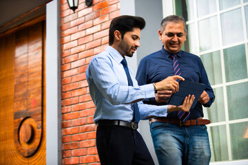 Indian corporate professionals walk with tablet, engaged in discussion outside office building