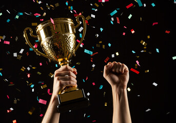 A moment of triumph with hands raising a gleaming gold trophy, celebrating a significant win with a fist pump and colorful confetti.