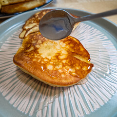 pancakes and honey Pour syrup over pancakes from silver syrup pitcher. Homemade pancakes in a gray plate are poured with a thin stream of slow motion honey. Medium plan.